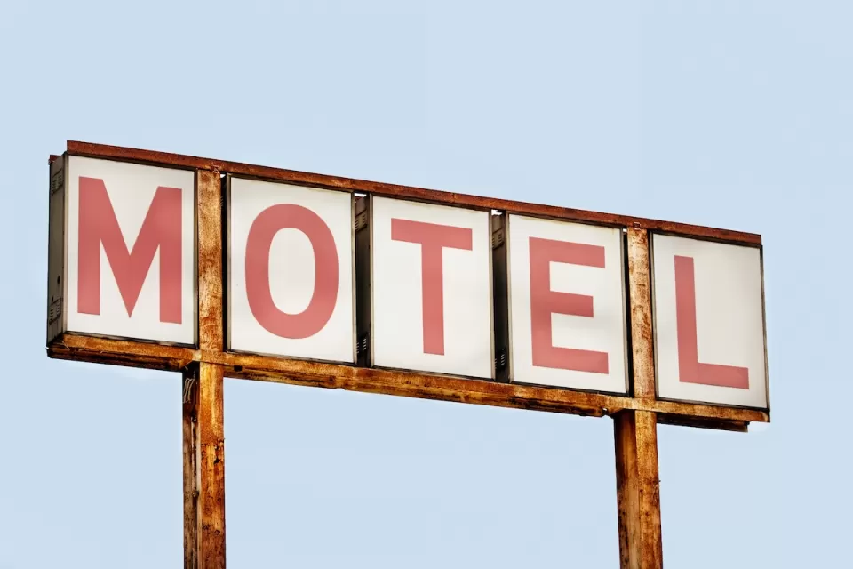 Close-up of faded old MOTEL sign with red letters on white placards against blue sky.